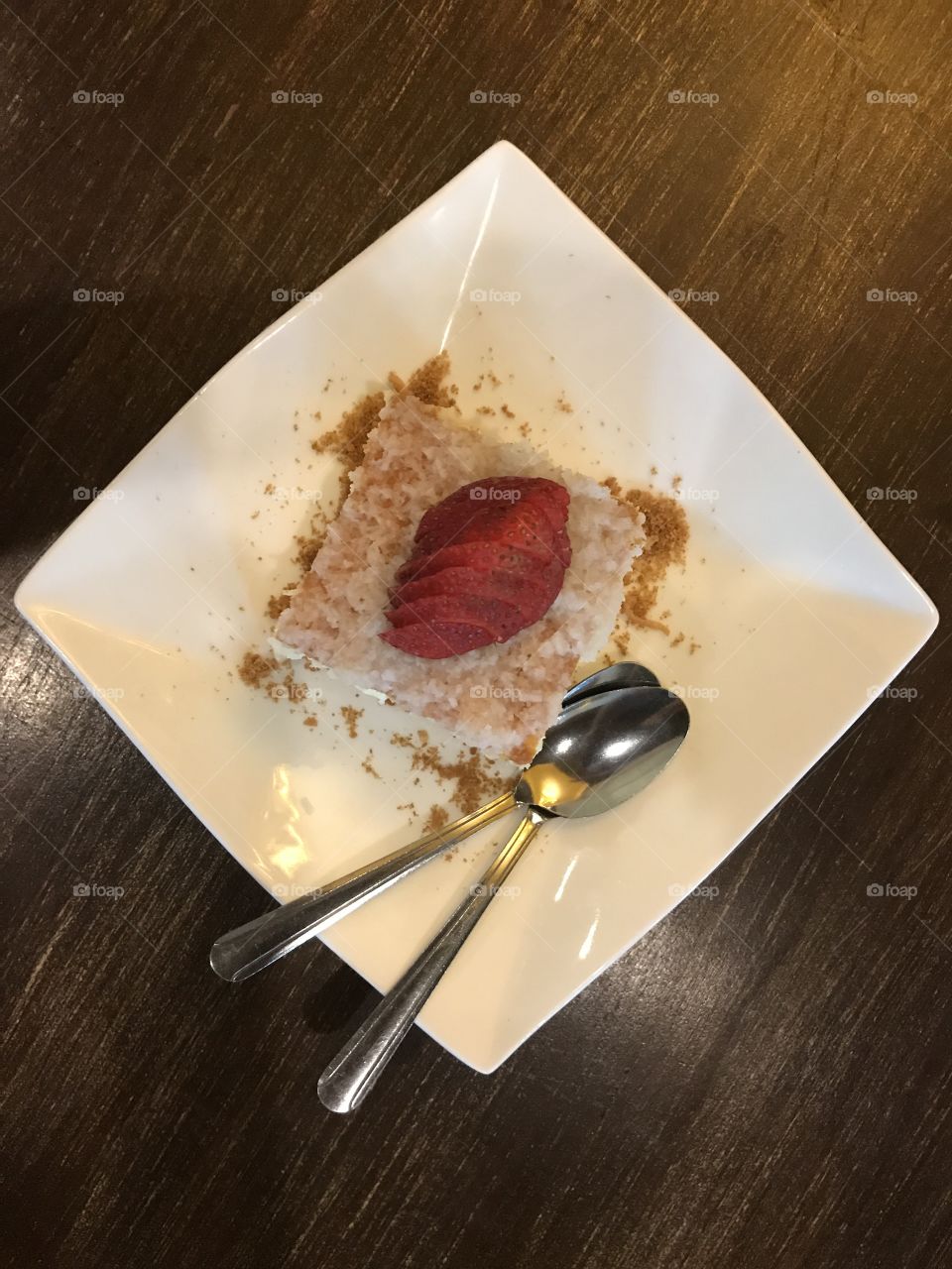 A good portion of square cheesecake topped with coconut flakes and sliced strawberry 