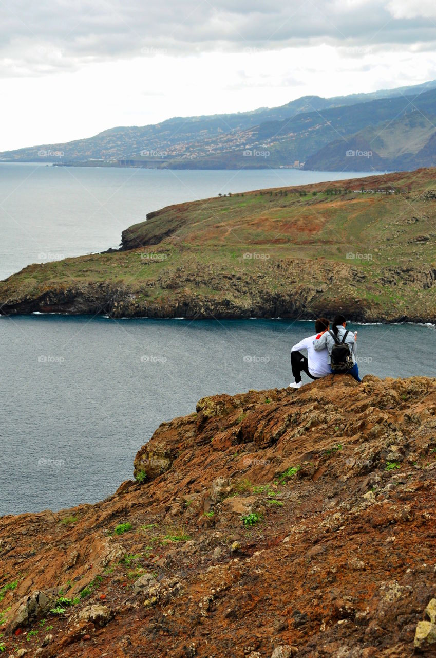 young couple sitting on the rocks admiring ocean and mountains landscape