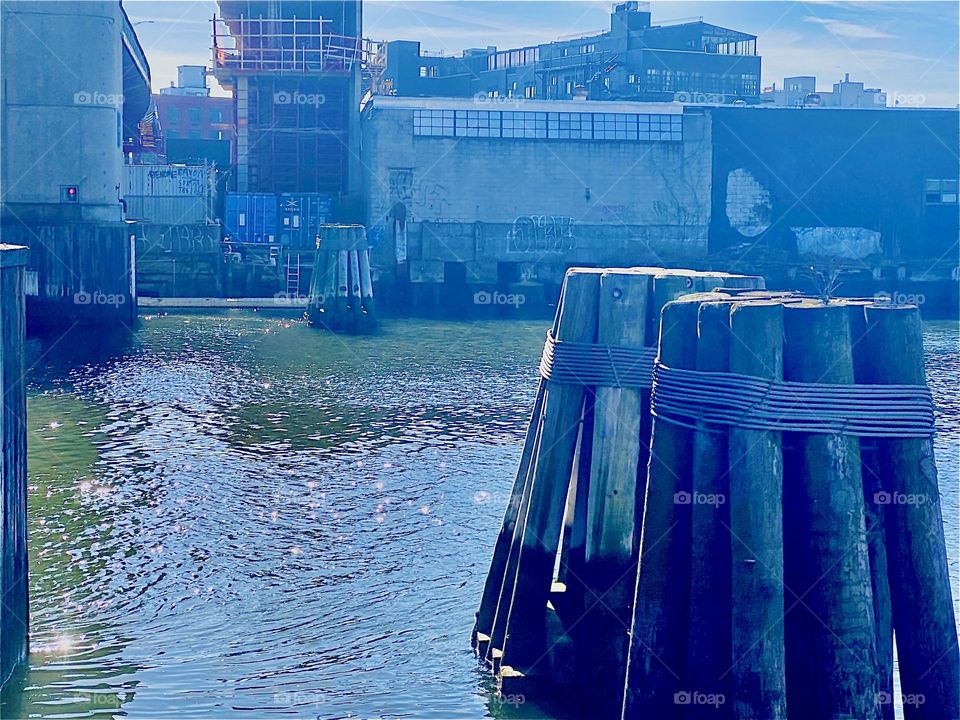 From beneath the “Pulaski Bridge” one gets a good look at the pilings in the water to mark the distance boats must clear in the E River. On a. sunny afternoon like this the ocean sparkles beautifully. 2023. Hypnotic Productions