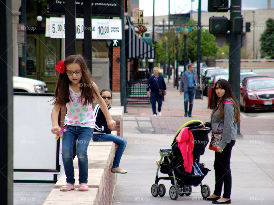 Playful City. Younger daughter playing as her mother and sister watch.