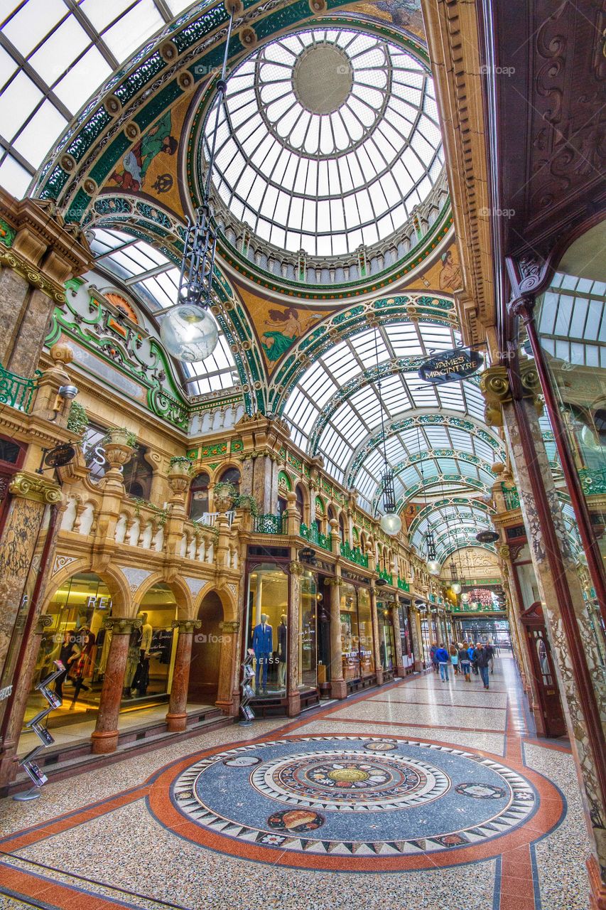 An ornate and decorative shopping arcade in Leeds with circular windows in the ceiling letting lots of light in.