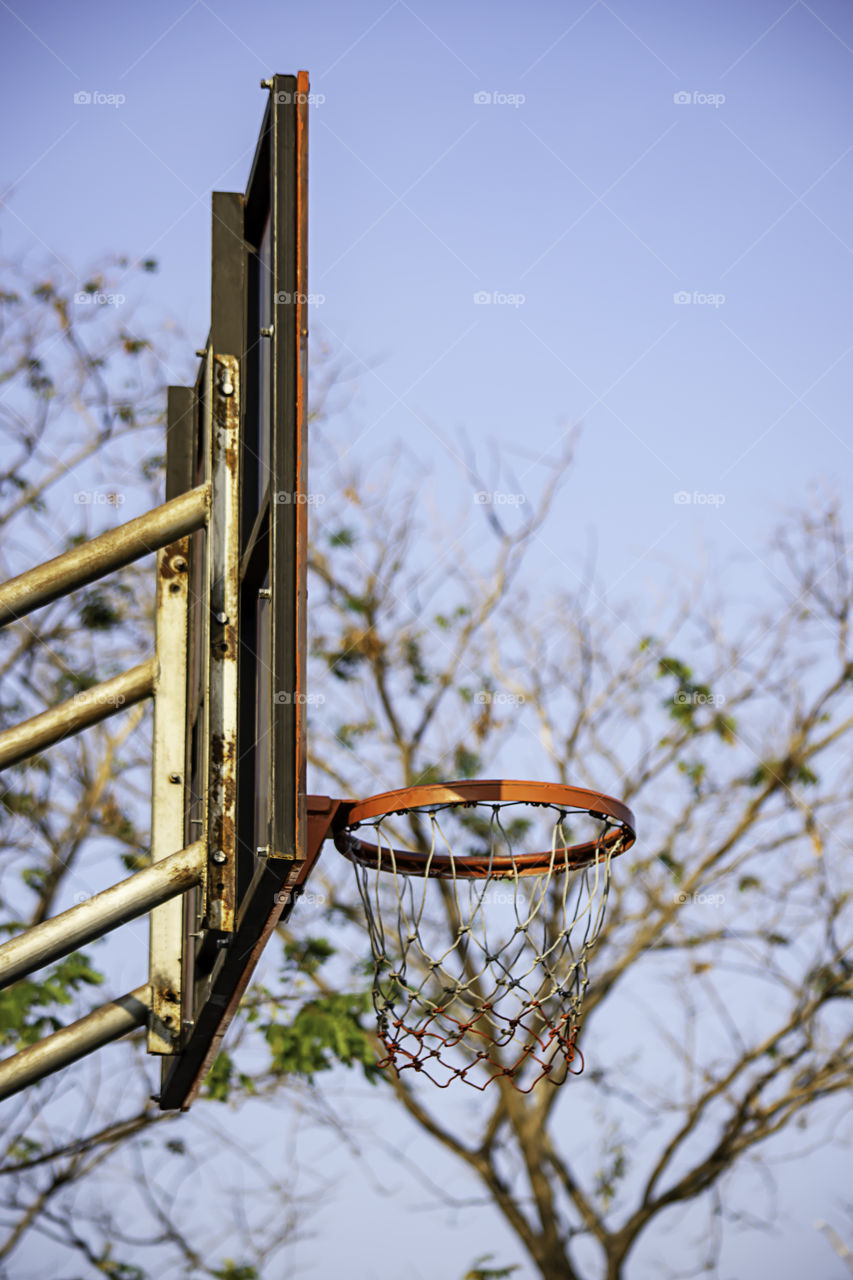 Basketball hoop background blurry tree and sky.