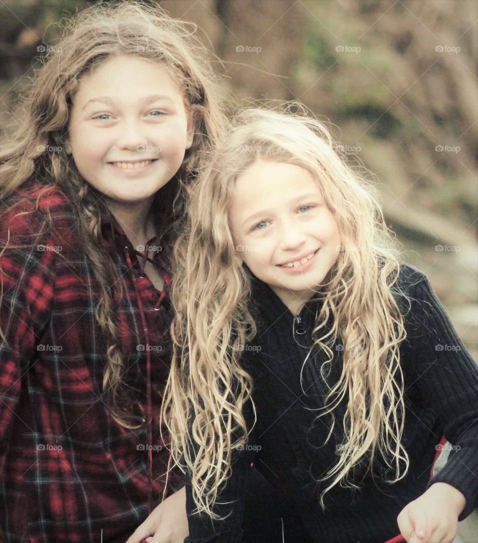Two beautiful sisters, with long flowing curls, smiling happily for the camera on a brisk autumn day. 