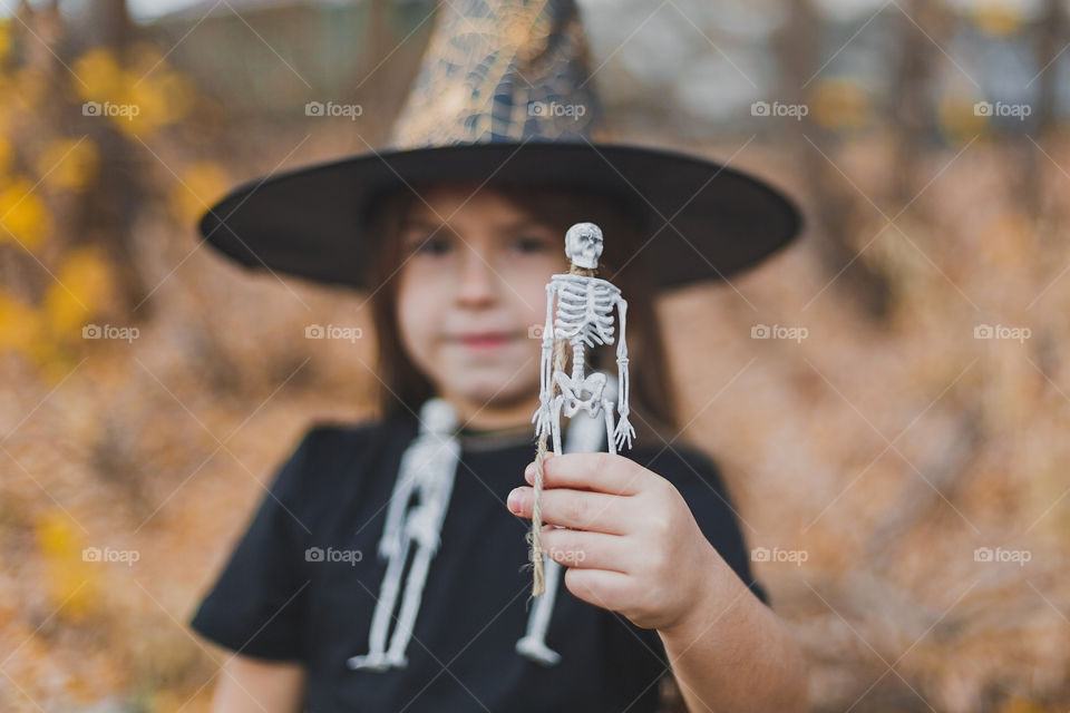 A girl in a witch costume on a green background holds a skeleton in her hands. Halloween concept