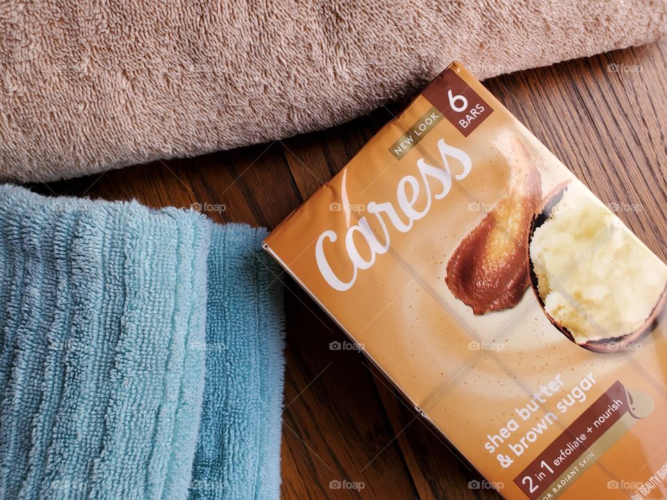 The new look Caress bar soap shea butter and brown sugar six pack, next to a tan towel and light blue towel on the left, on a wood surface.