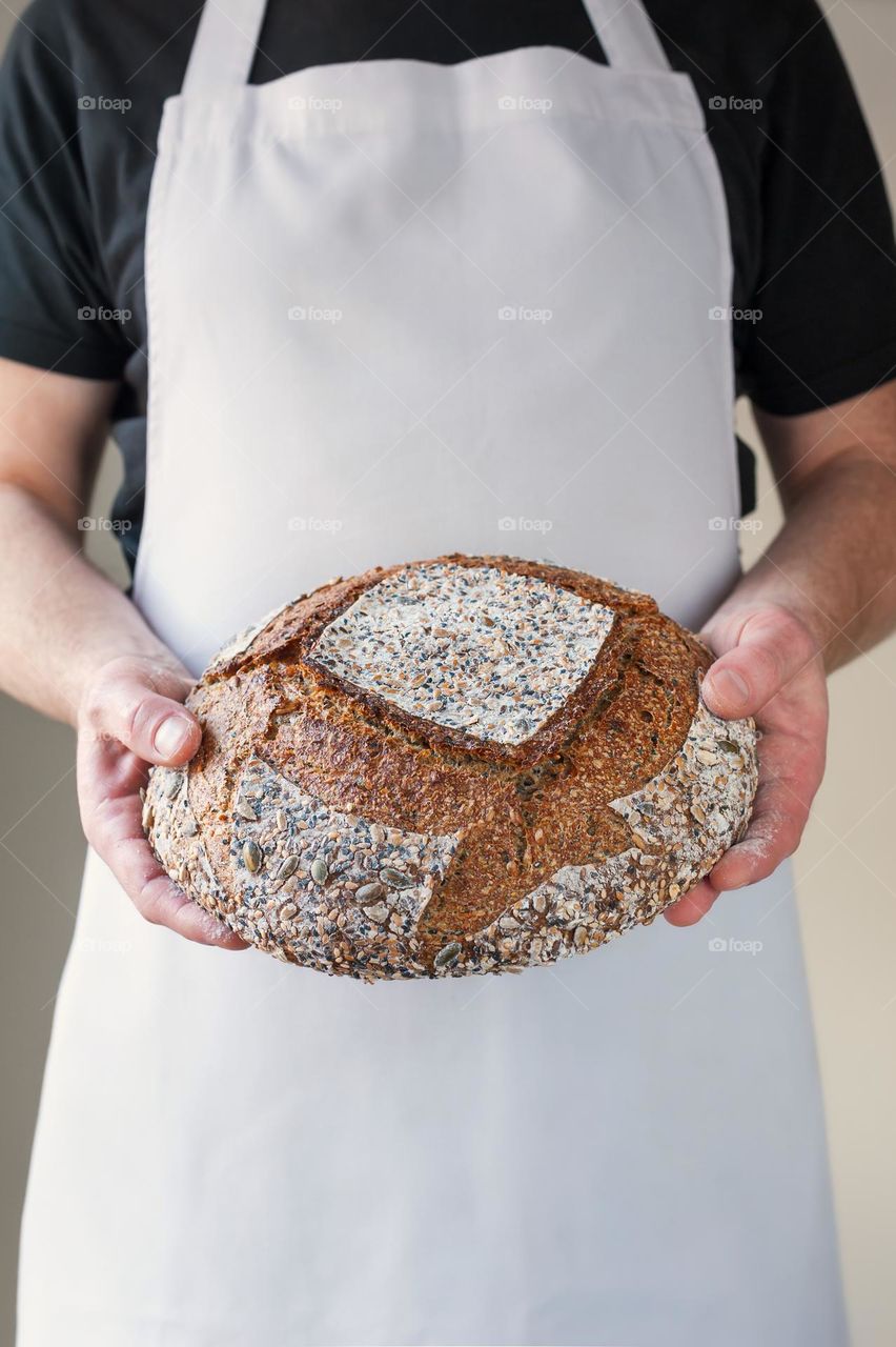 Close-up at bakers hands holding a loaf of sourdough bread in front of him.