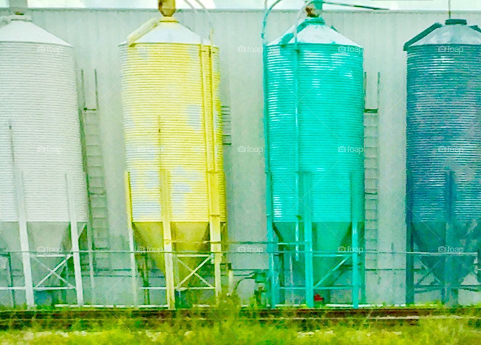 Pastel colored metal water tanks with ladders at a warehouse by the railroad 