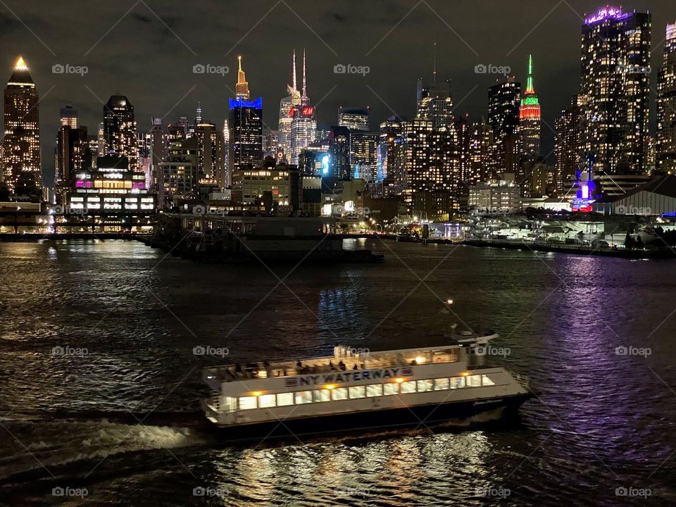 The New York City skyline and a ferry at night viewed from the Hudson River