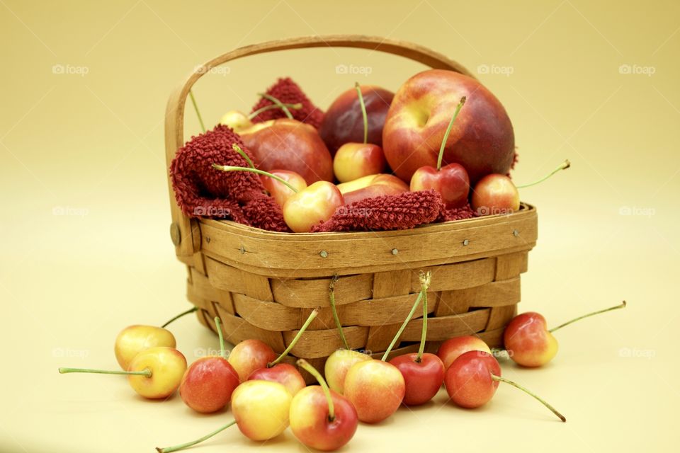 Fruits! - Nectarines And Rainer cherries in a wooden basket against a yellow background 