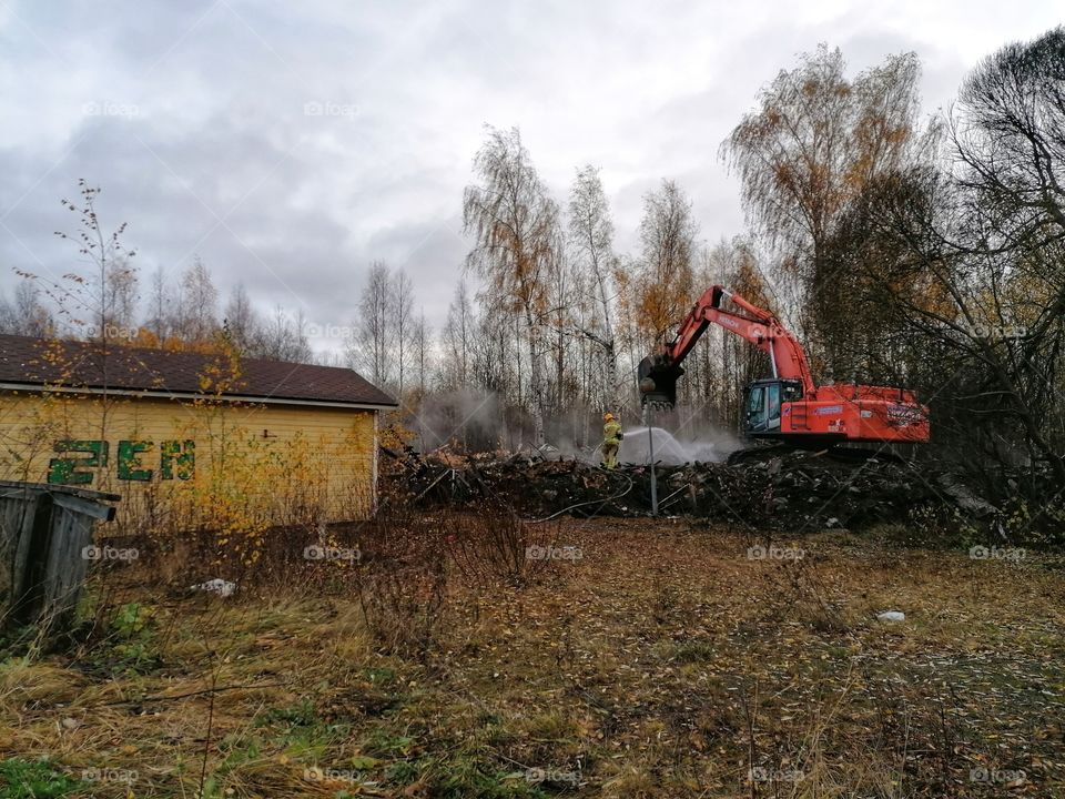 A firefighter and an excavator extinguishing a fire in a large building.