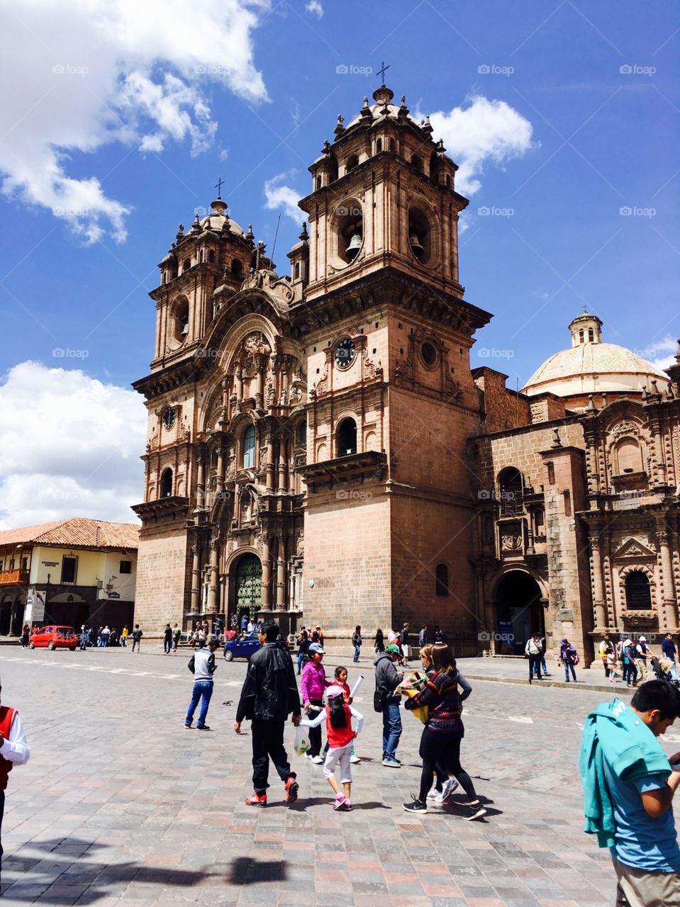 People gather around an old church sitting on Cuzco’s main square on a sunny day. 
