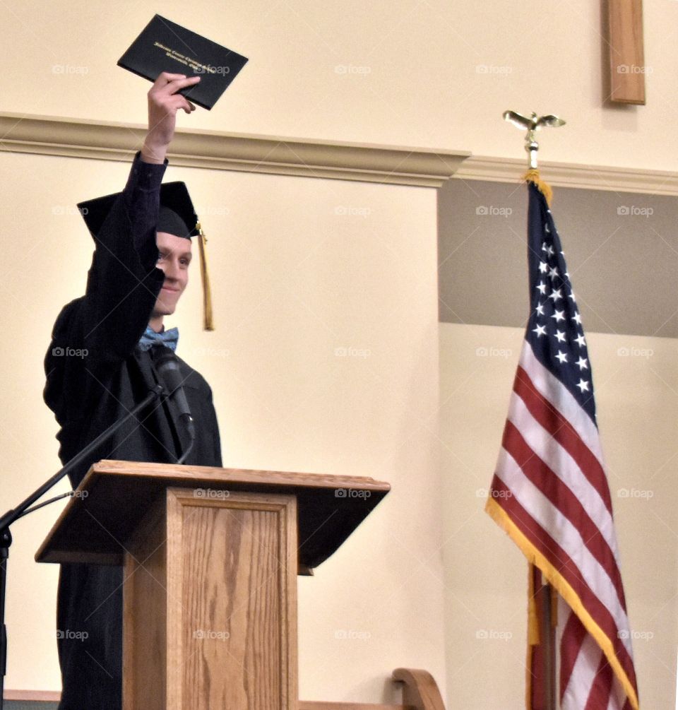 Graduate holding up his diploma, standing by the American flag 