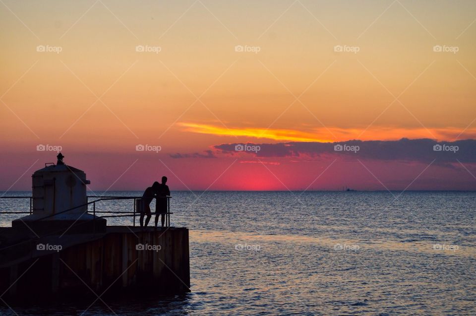 Two peoples standing on lighthouse at sunset
