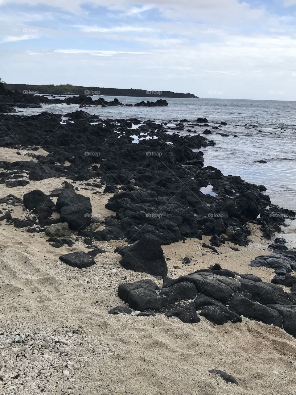 Black volcanic rock on sandy beach. Maui