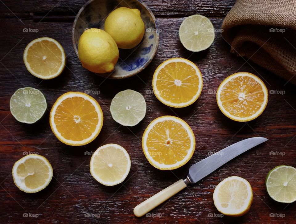 Orange, lemon and limes cut open and displayed on rustic wood table with knife and bowl of lemons.