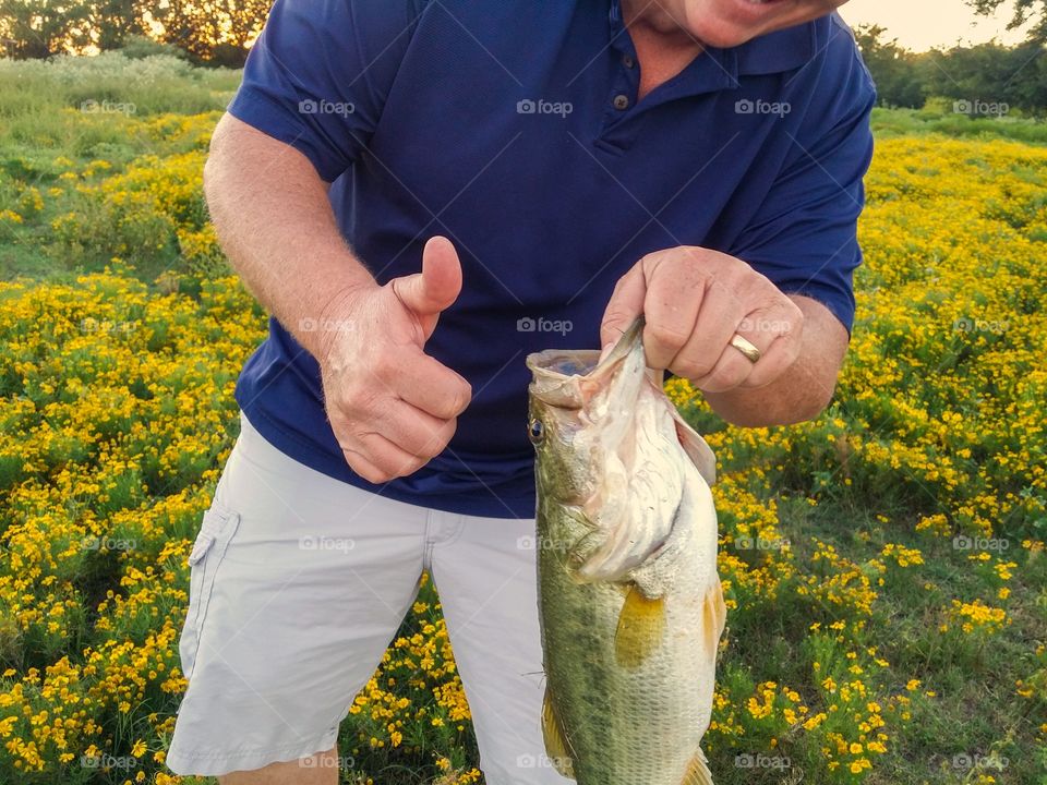 Staying in good shape with a hobby you love and takes you outside a man with a big smile and thumbs up to a big mouth bass he just caught being in nature