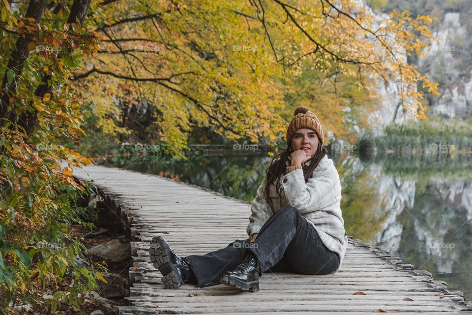 Girl sitting on wooden walkway under autumn trees by a lake