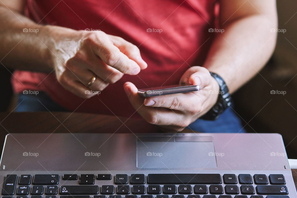 Man using smartphone working on laptop sitting at a desk