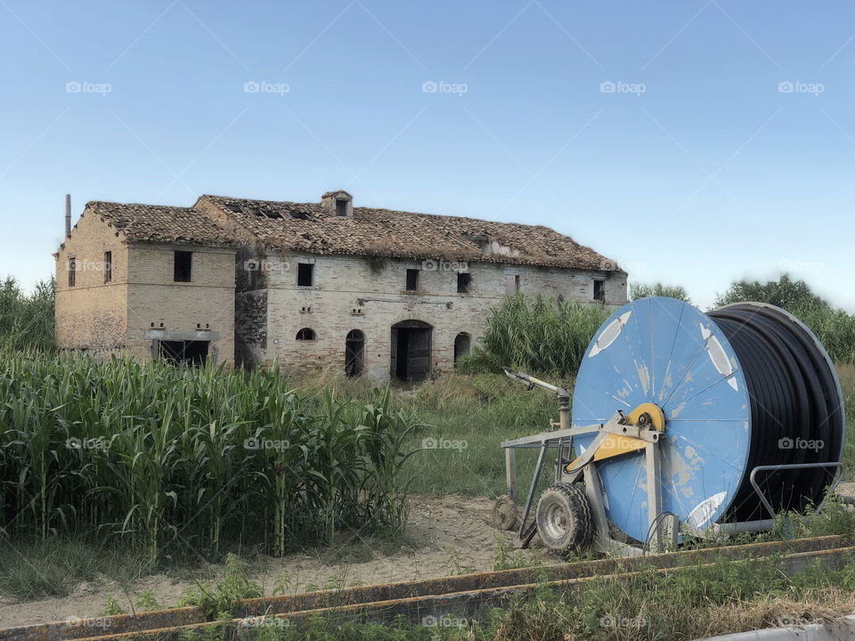 Irrigation machine front of a typical marche region country house abandoned in the Natural Park of Sentina, Italy

