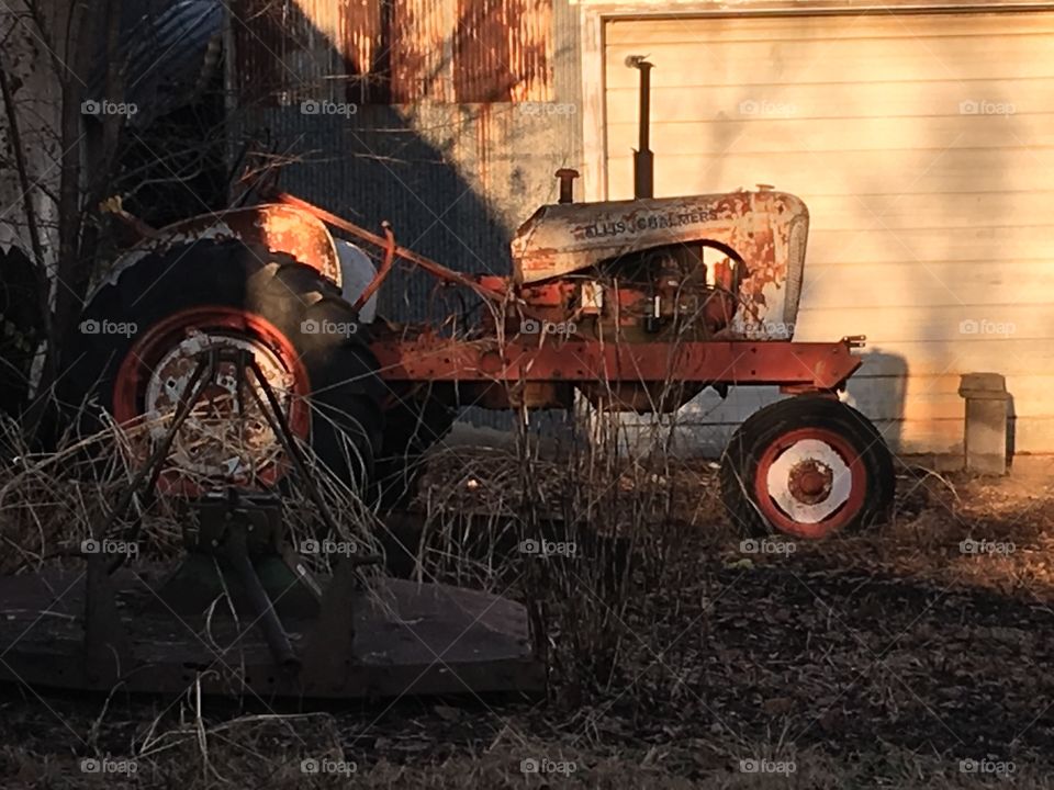 An old tractor just sitting and getting rusty behind a building probably still runs.