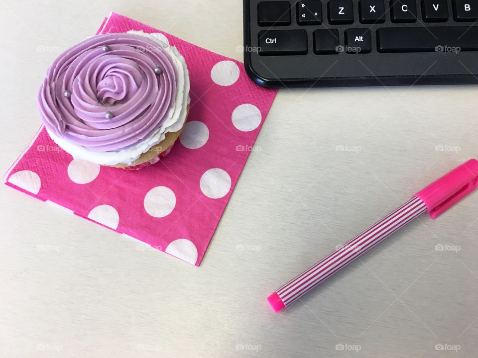 Pink cupcake on office desktop with keyboard snacking at work or celebrating success at work conceptual background 