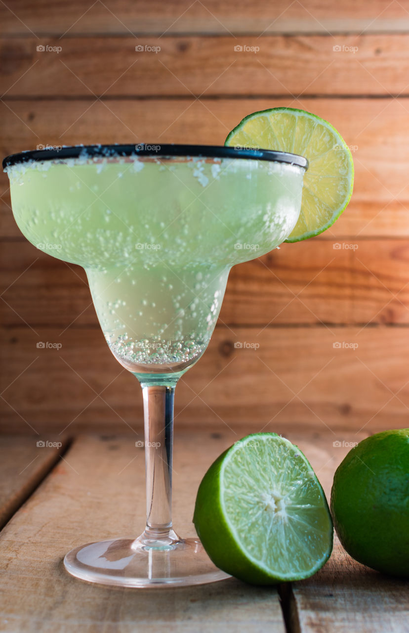 mock margarita in margarita glass with salt and lime on the rim and sitting next to a sliced lime on a wood table with a wood background