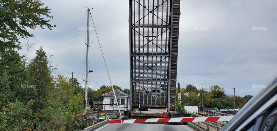 a tall sailboat on the Dismal Swamp Canal prepares to pass the raised drawbridge as the cars wait