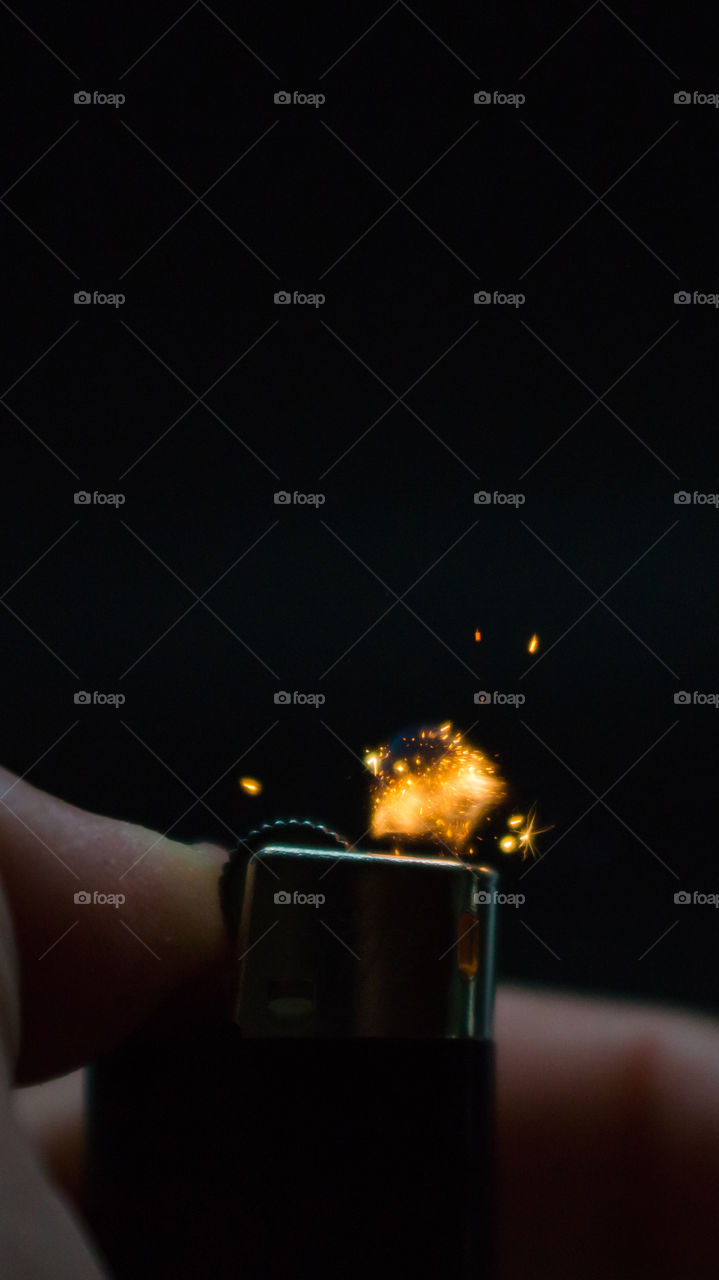 A person has lighters in his hands and he lights it through a flint wheel, the lighter ignites, sparks and fire appear, close-up on a black background.