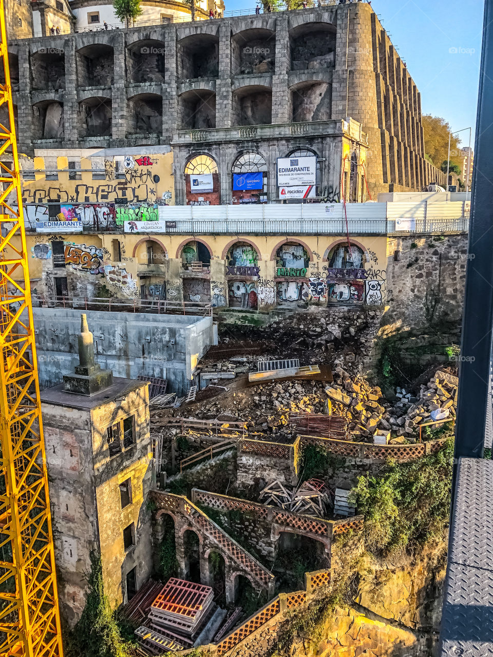 A scene of demolition and dereliction in Porto, framed by the metal structures of a crane and a bridge on either side