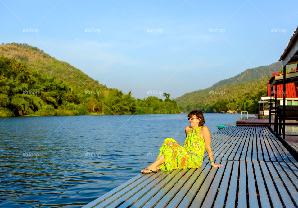 Woman sitting on deck at lake near mountain