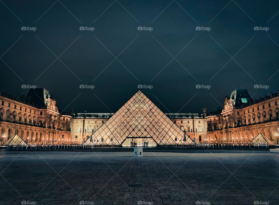 Louvre, Paris at midnight lit up in golden hue against deep blue skies.