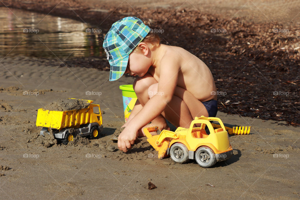 Little boy's playing on the beach with yellow toys