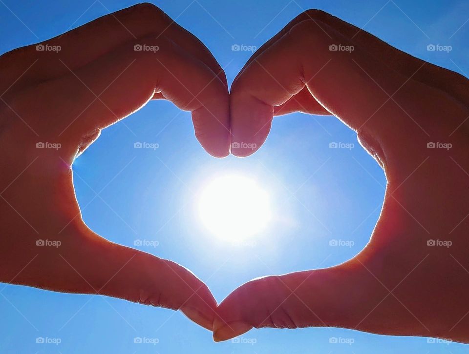 Hands folded in the shape of a heart envelop the blue sky with sun💙🌞💙