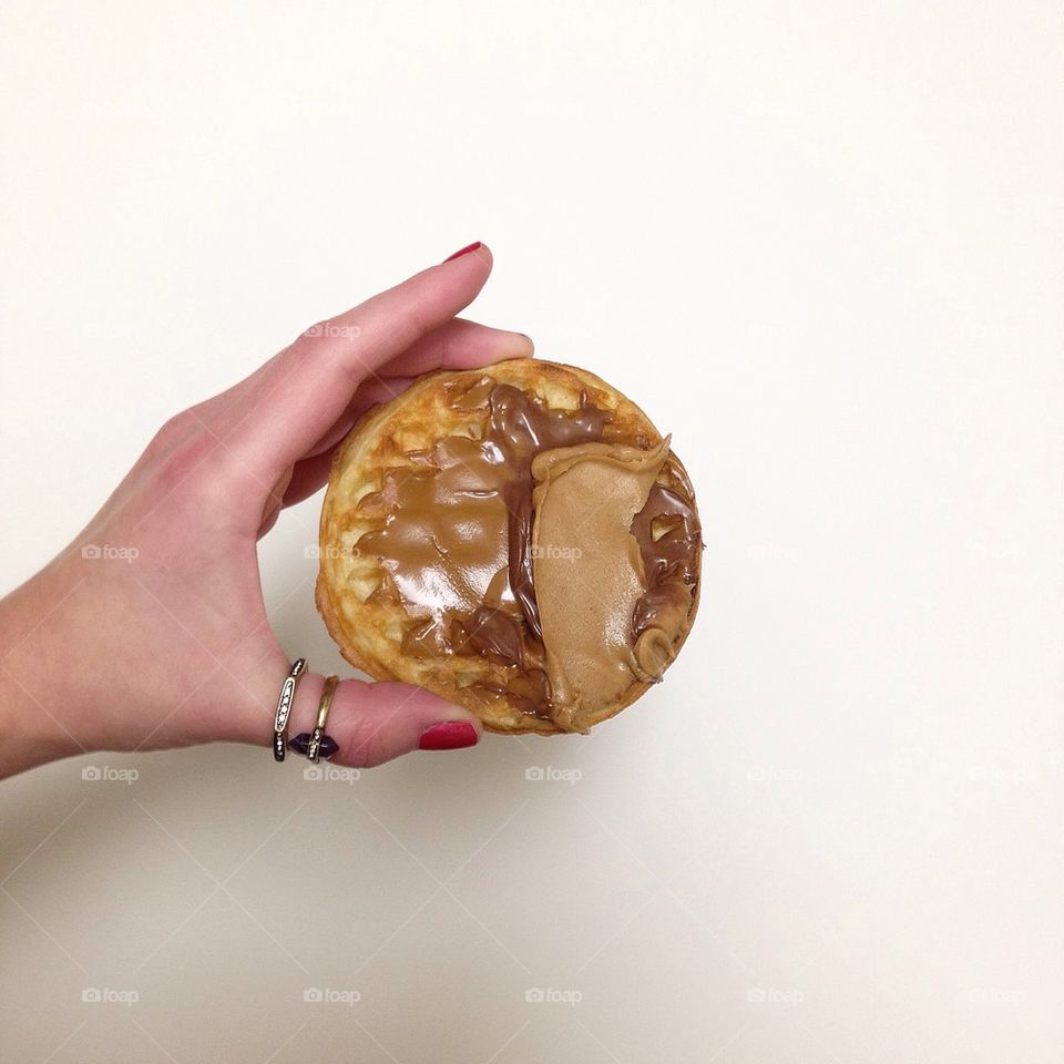 Hand with rings holding waffle with Nutella cookie butter and peanut butter