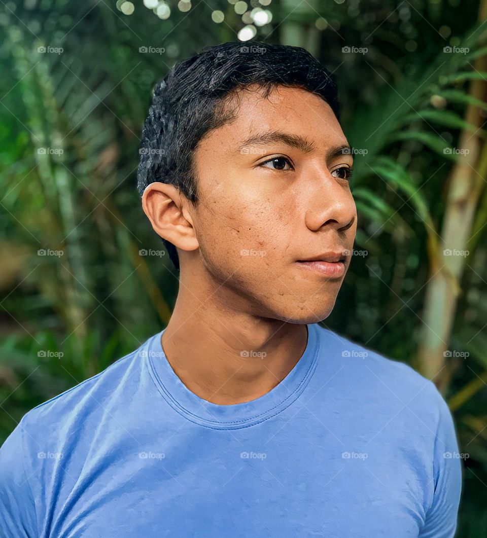 dark-skinned man in porfile, with pimples and pimple scars, with vegetation background