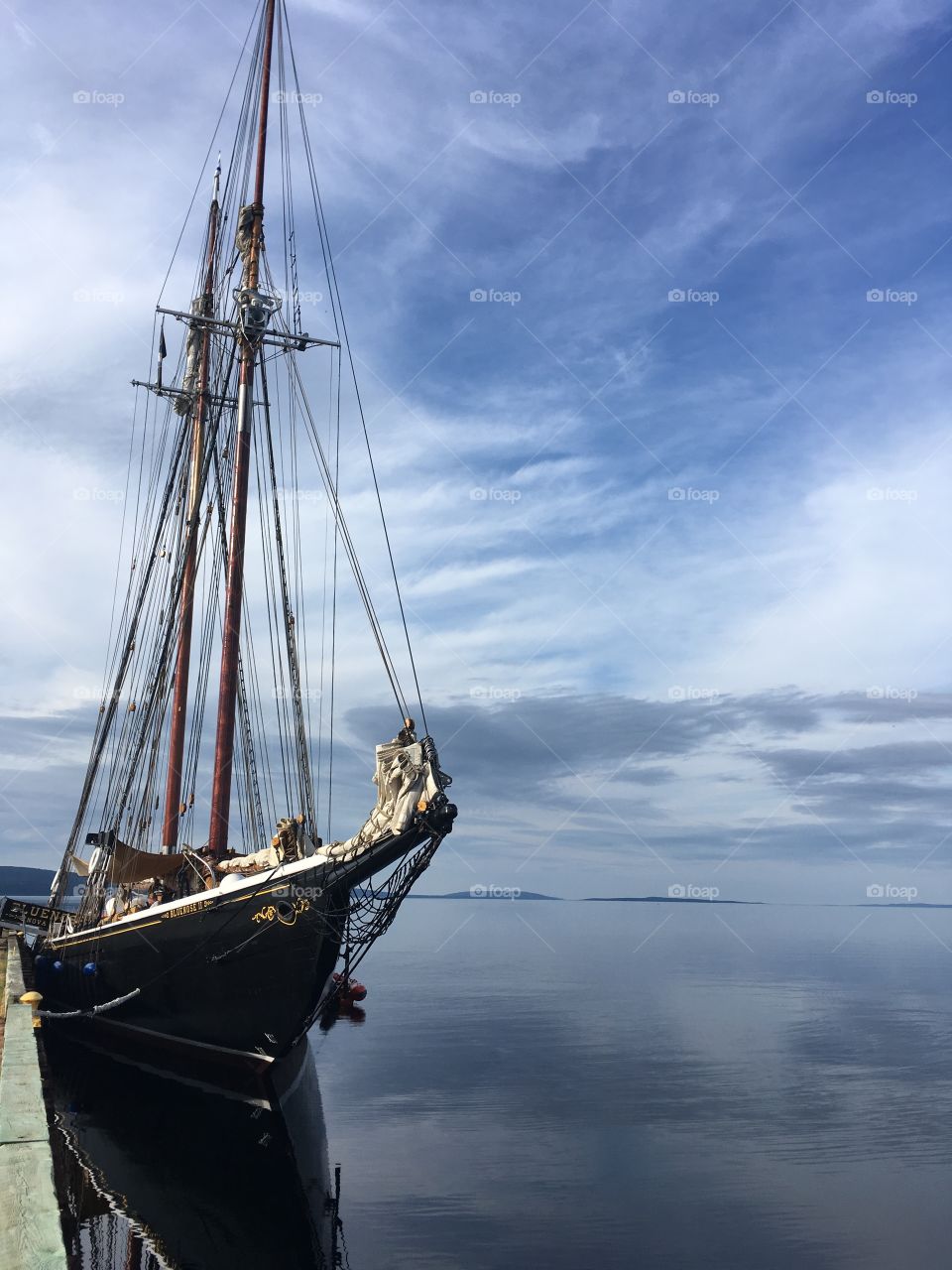 The legendary Bluenose II sailboat docked in a lake of calm water. 