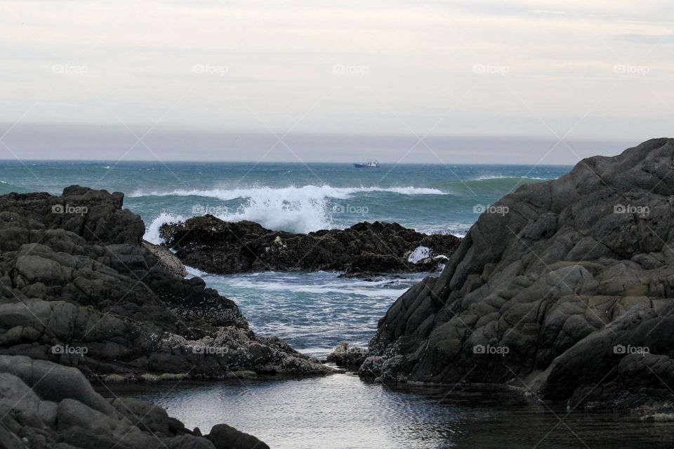 Waves crashing against the rocks with a chokka boat in the distance