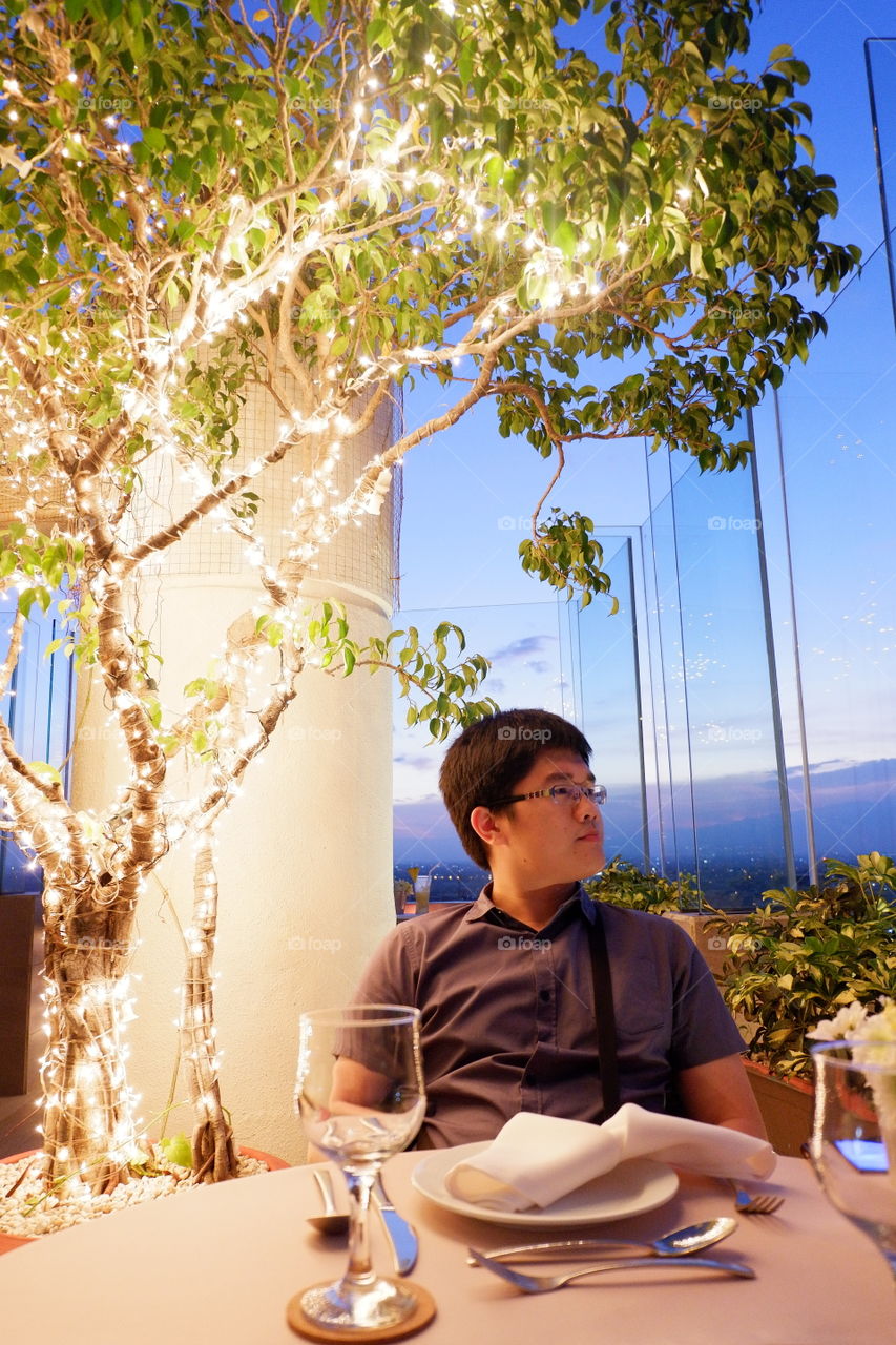 Asian man sitting at table with illuminated tree at restaurant