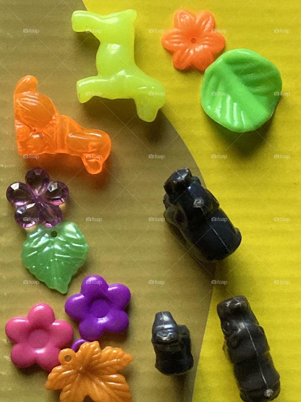 Arte  montada com objetos bem coloridos sobre uma superfície bem amarela. Arte de criança usando objetos de plástico.