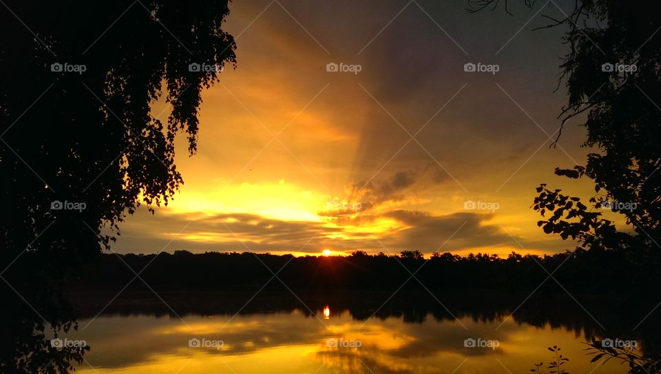 Silhouetted trees and dramatic sky reflecting on lake
