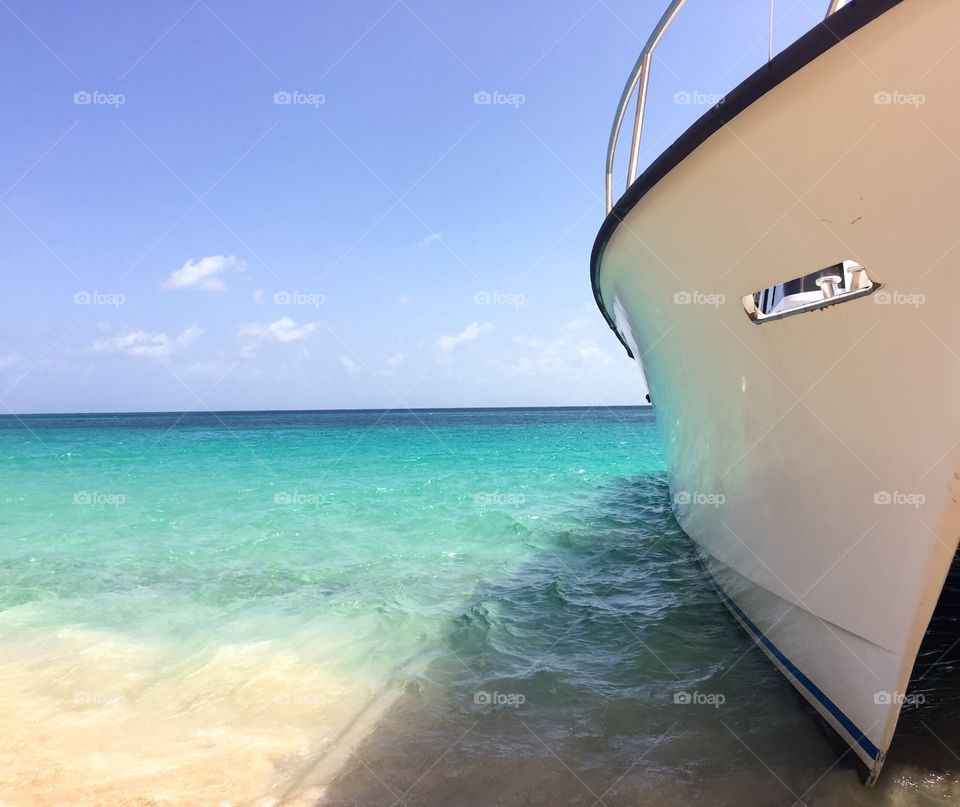 Caribbean beach with a boat in the crisp turquoise water. Few clouds in the blue sky.  