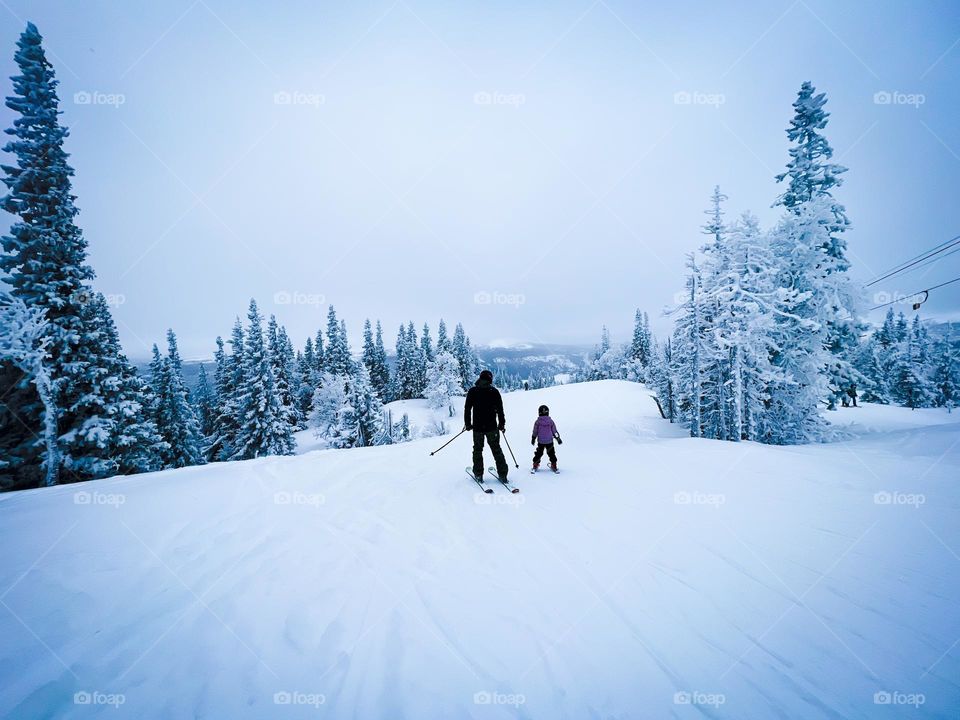 Adult and child on ski slope in white winter wonderland scenery