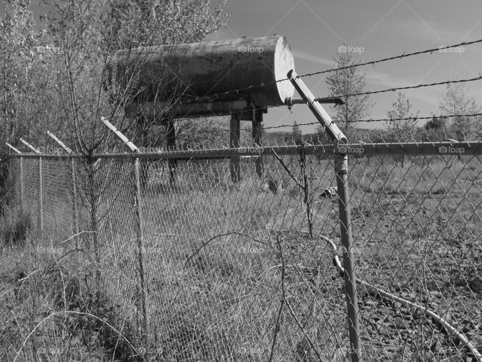 An old industrial container on metal legs stands at the edge of a field next to a foreboding fence in Western Oregon on a spring day. 