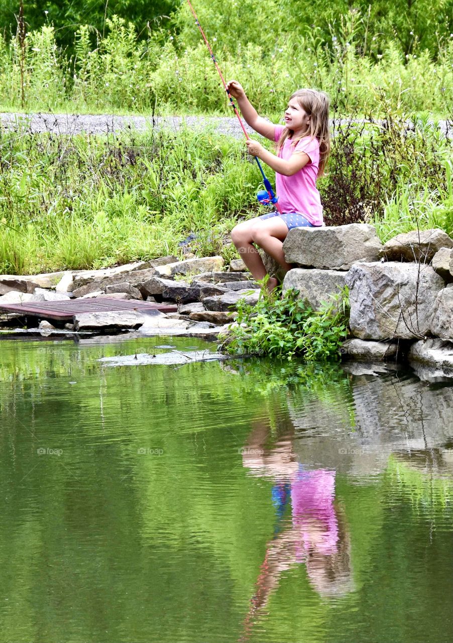 Young girl fishing in a pond with her reflection in the water