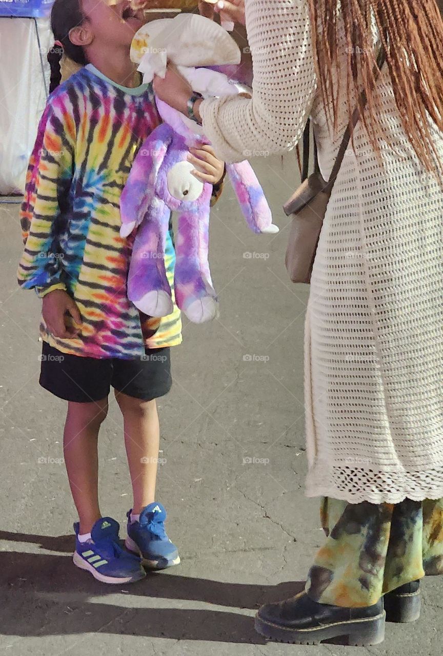 A mother feeding her daughter a treat at a county fair on a Summer evening