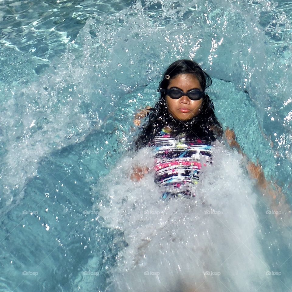 Girl making a big splash in a pool by falling in backwards 