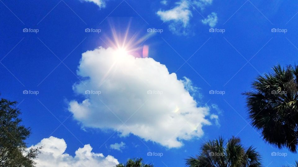 A beautiful cloud with a sun flare peaking over looking down at the earth. I love the rich blue sky!