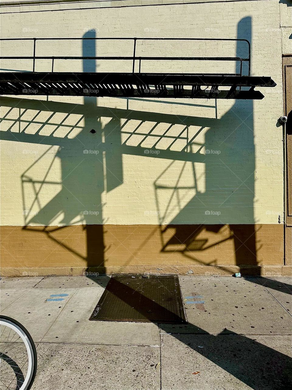 Modern art is created here on the facades of “Jefferson St” off “Broadway” in “Bushwick”, Bklyn when the afternoon sun casts shadows from interlinked shapes of the “M” train overpass and billboards at “Myrtle Ave” station. 2024. Hypnotic Productions