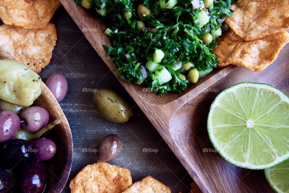 Healthy green salad with lime, olives and popped protein chips in wooden serving bowls.