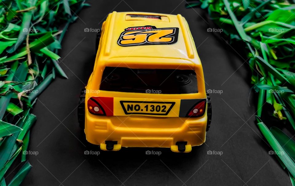 yellow car toy, on an asphalt road path, with trees around, made with grass and leaves
